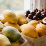 Baskets of mangoes, cherries and passionfruit on a summer produce table in afternoon light
